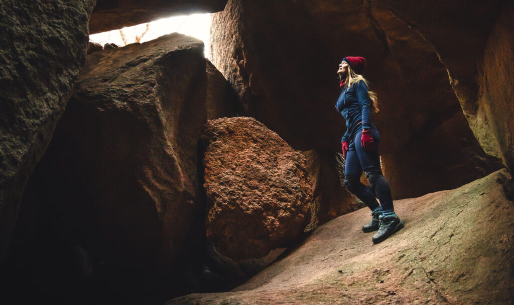 Female hiker in cave, wearing RBX leggings, Clorts hiking boots, Ollie Arnes hoodie.