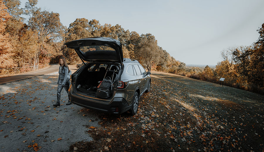 Woman walking around Subaru Outback with back hatch open parked at Picnic Point in Brown County State Park.
