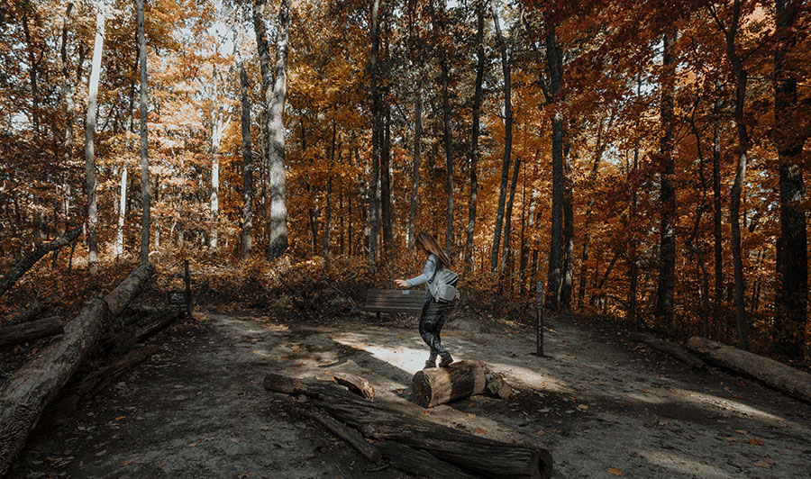 Woman hiker balancing on a log at a trail junction along Ayne's Loop at Brown County State Park.